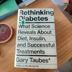Book laying on a desk surrounded by a stack of blank index cards and a coaster. The title of the book is Rethinking Diabetes, by Gary Taubes.
